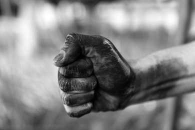 Photo of Dirty worker clenching fist on blurred background, closeup of hand. Black and white effect