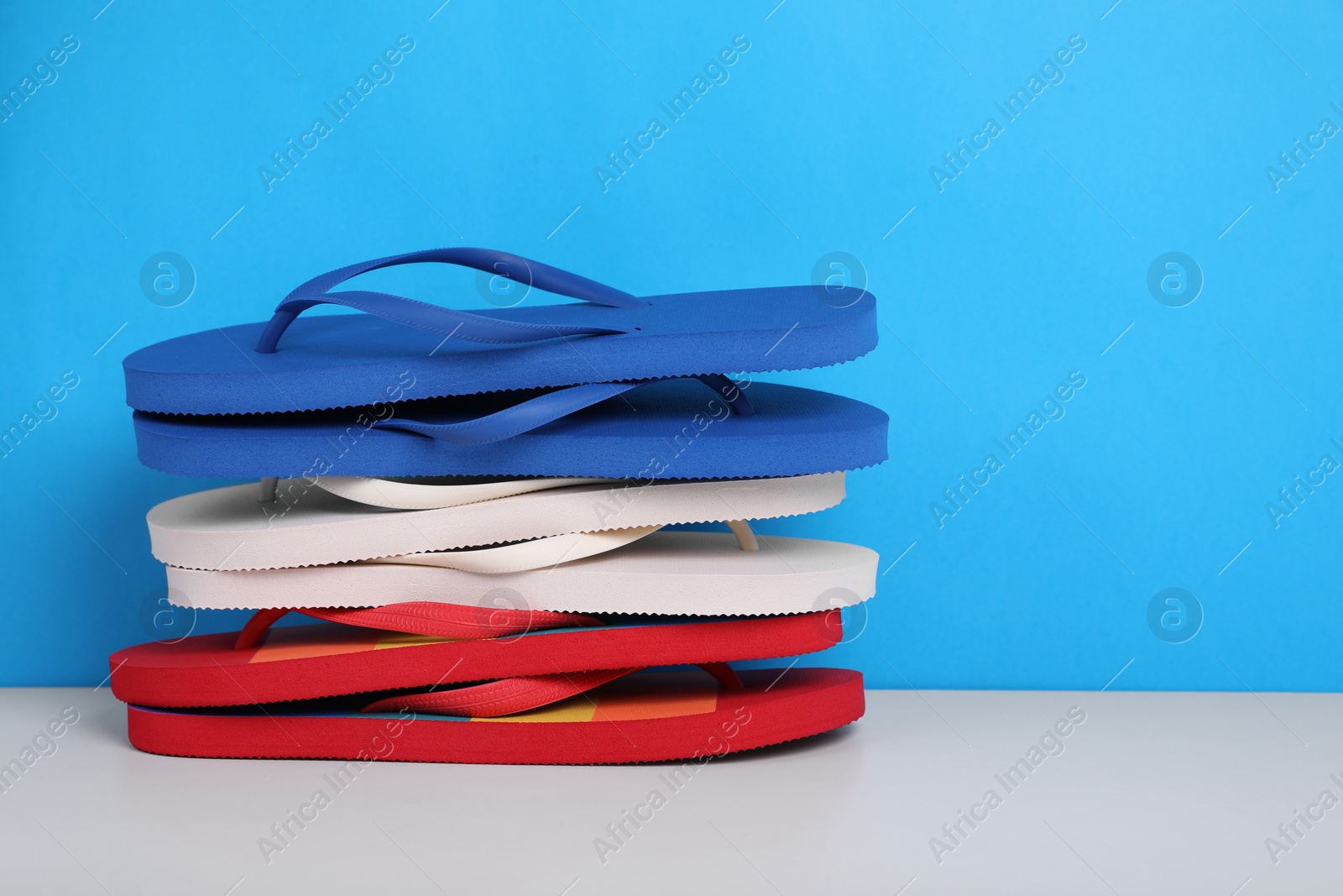 Photo of Stack of different flip flops on white table against light blue background