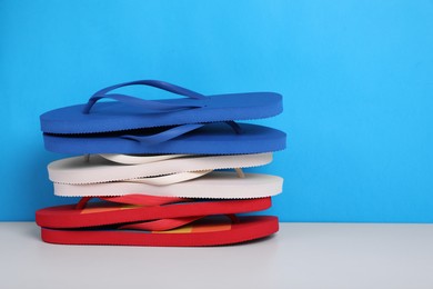 Stack of different flip flops on white table against light blue background