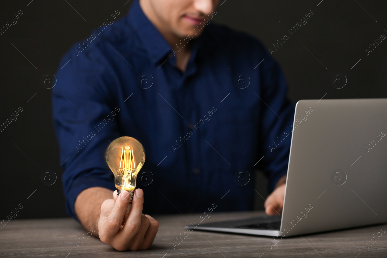 Photo of Glow up your ideas. Closeup view of man holding light bulb while working at wooden desk, space for text