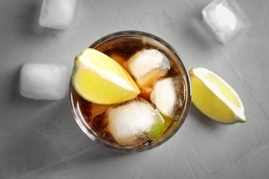 Photo of Glass of cocktail with cola, ice and cut lime on light background, flat lay