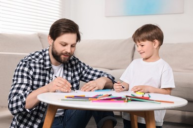 Photo of Dad and son drawing together at coffee table indoors
