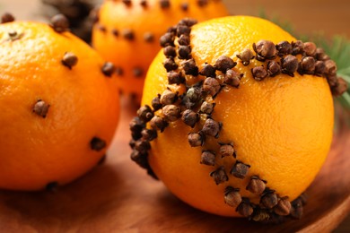 Photo of Pomander balls made of tangerines with cloves on wooden plate, closeup