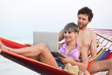 Photo of Young couple resting with laptop in hammock on beach