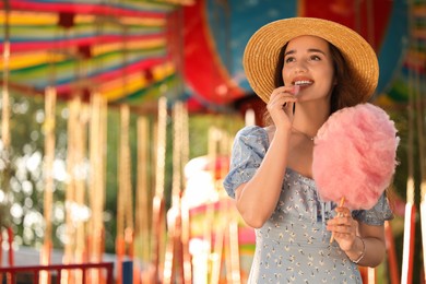 Photo of Beautiful young woman eating cotton candy at funfair, space for text