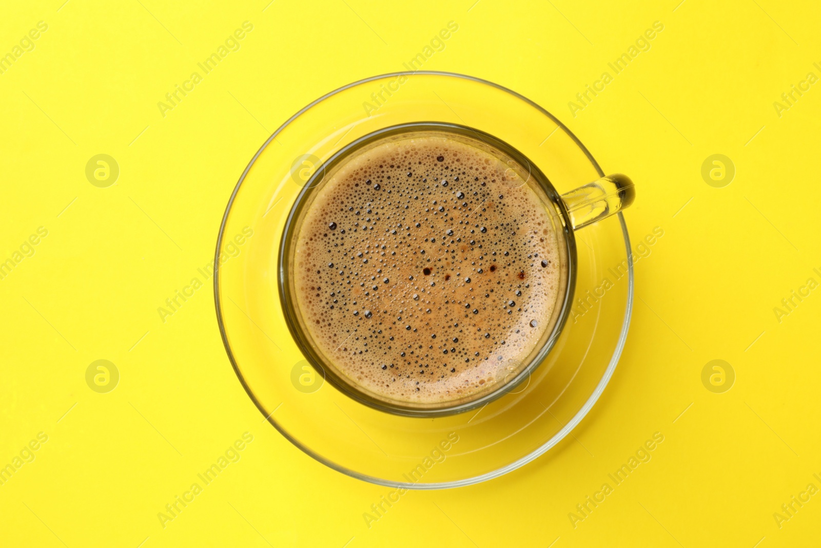 Photo of Aromatic coffee in glass cup on yellow background, top view