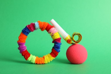 Clown nose, party blower and fluffy wires on green background