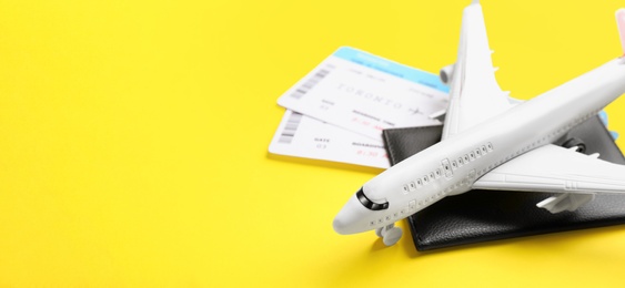 Toy airplane and passport with tickets on yellow background, closeup. Space for text