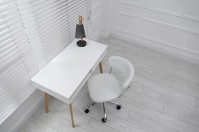 Photo of Stylish workplace with white desk and comfortable chair near window indoors. Interior design