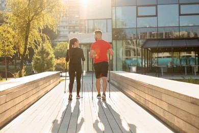 Photo of Couple practicing Nordic walking with poles outdoors on sunny day, back view