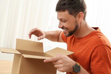 Happy man opening parcel indoors. Internet shopping