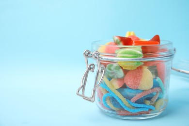 Photo of Tasty colorful candies in glass jar on light blue background, closeup. Space for text