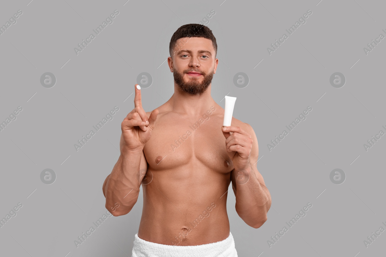 Photo of Handsome man with tube of body cream on light grey background