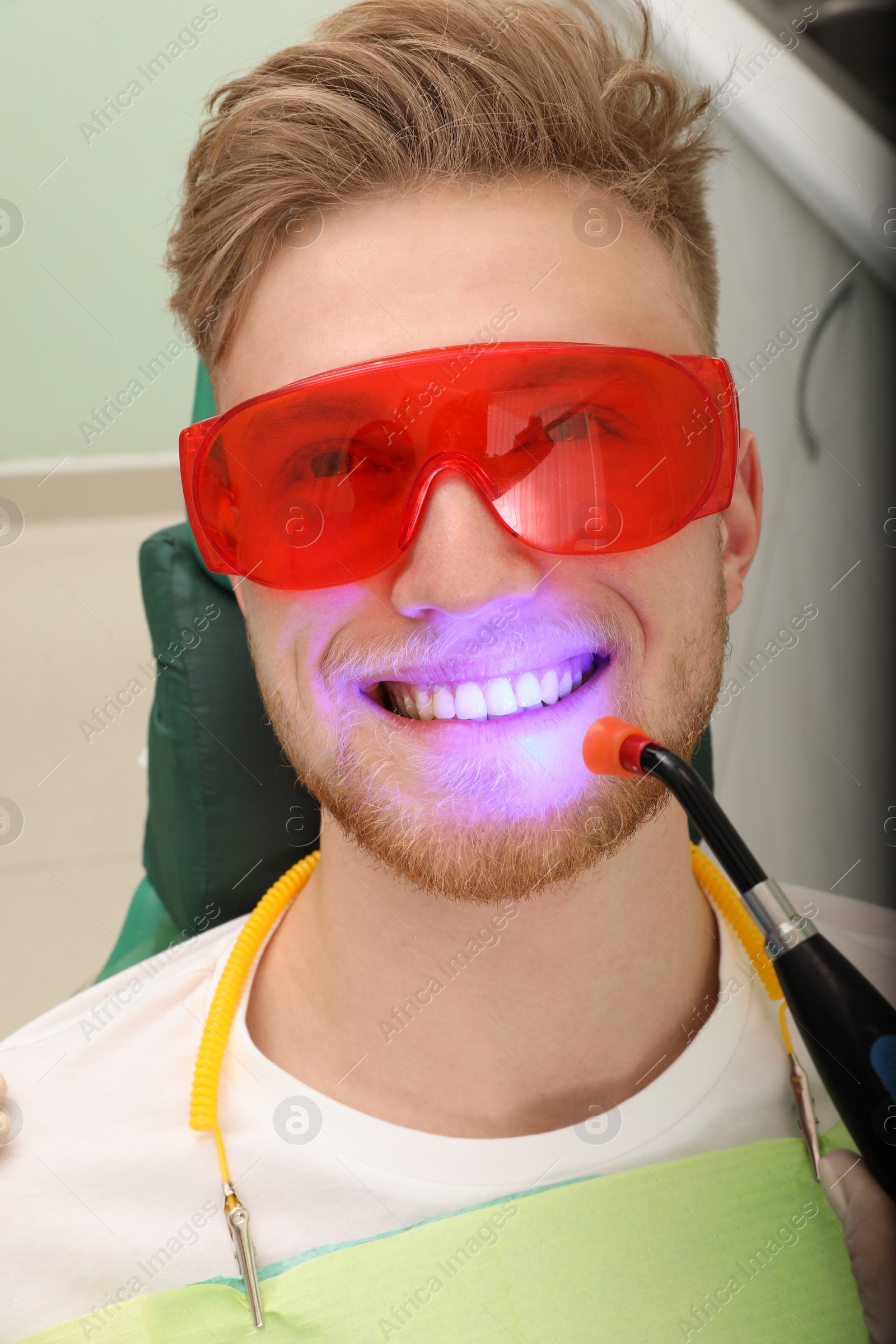 Photo of Young patient undergoing teeth whitening procedure in clinic. Visit dentist