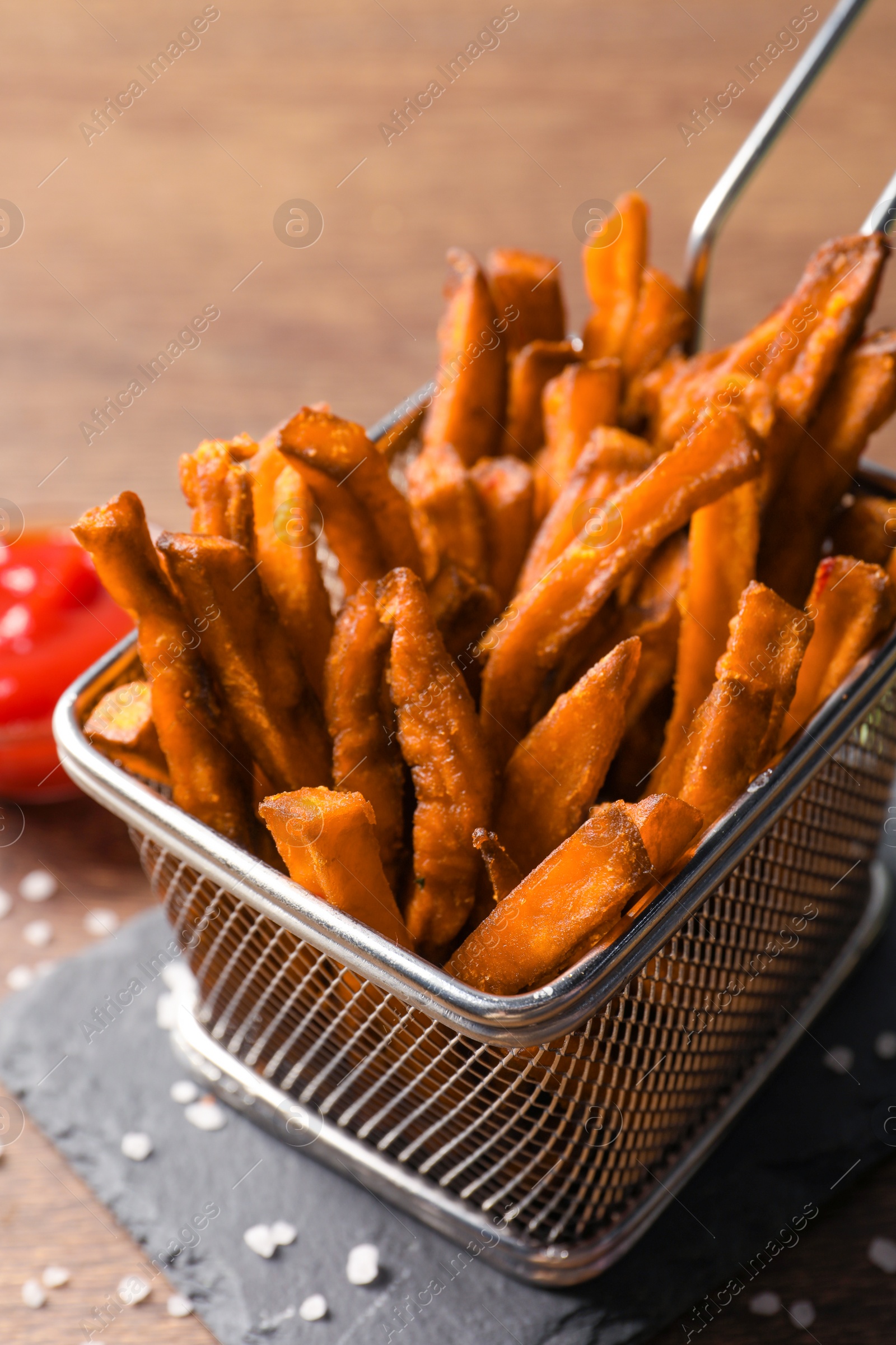 Photo of Frying basket with sweet potato fries on wooden table, closeup