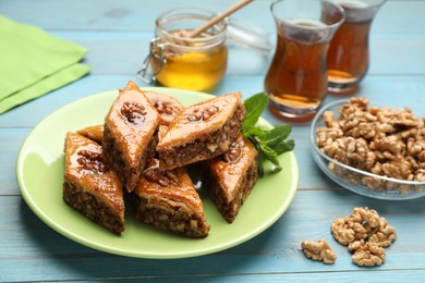 Photo of Delicious sweet baklava with walnuts and mint on turquoise wooden table