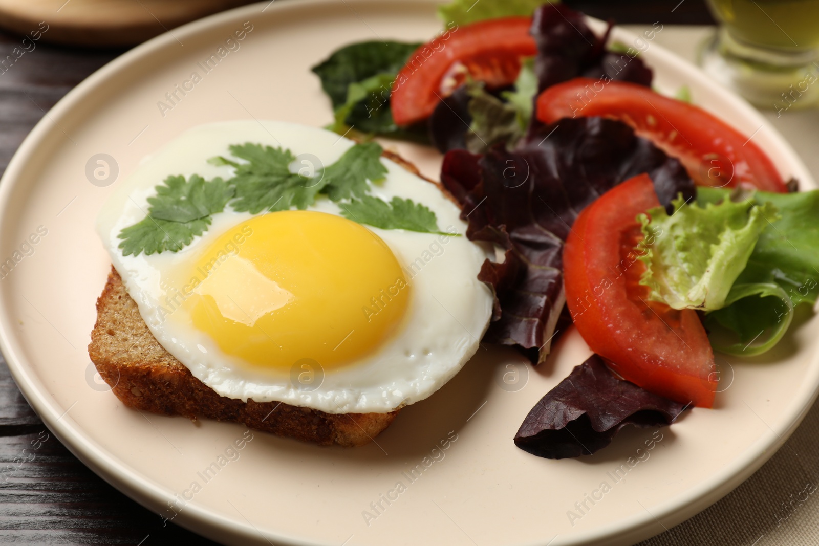 Photo of Plate with tasty fried egg, slice of bread and salad on wooden table, closeup