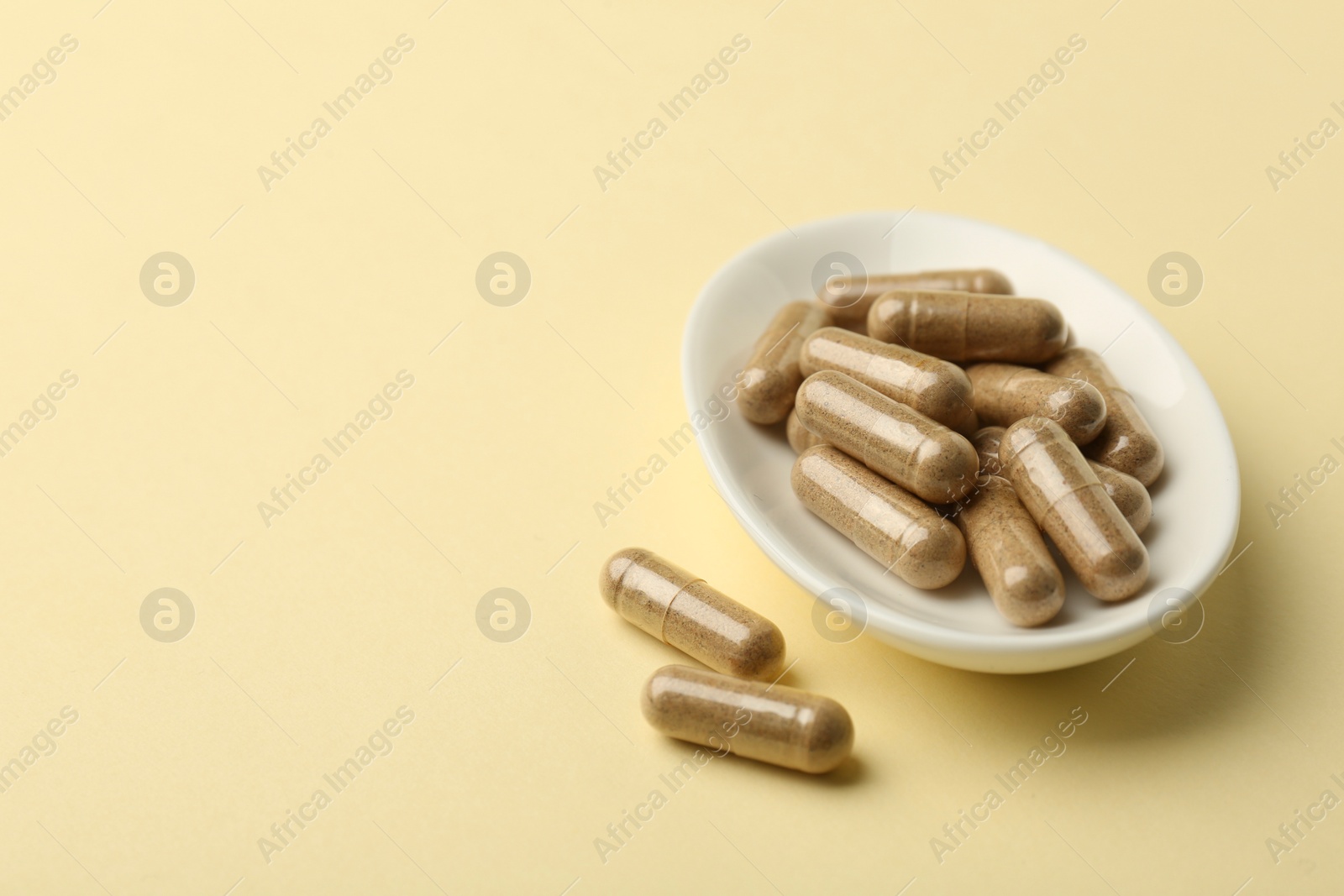 Photo of Vitamin capsules on pale yellow background, space for text