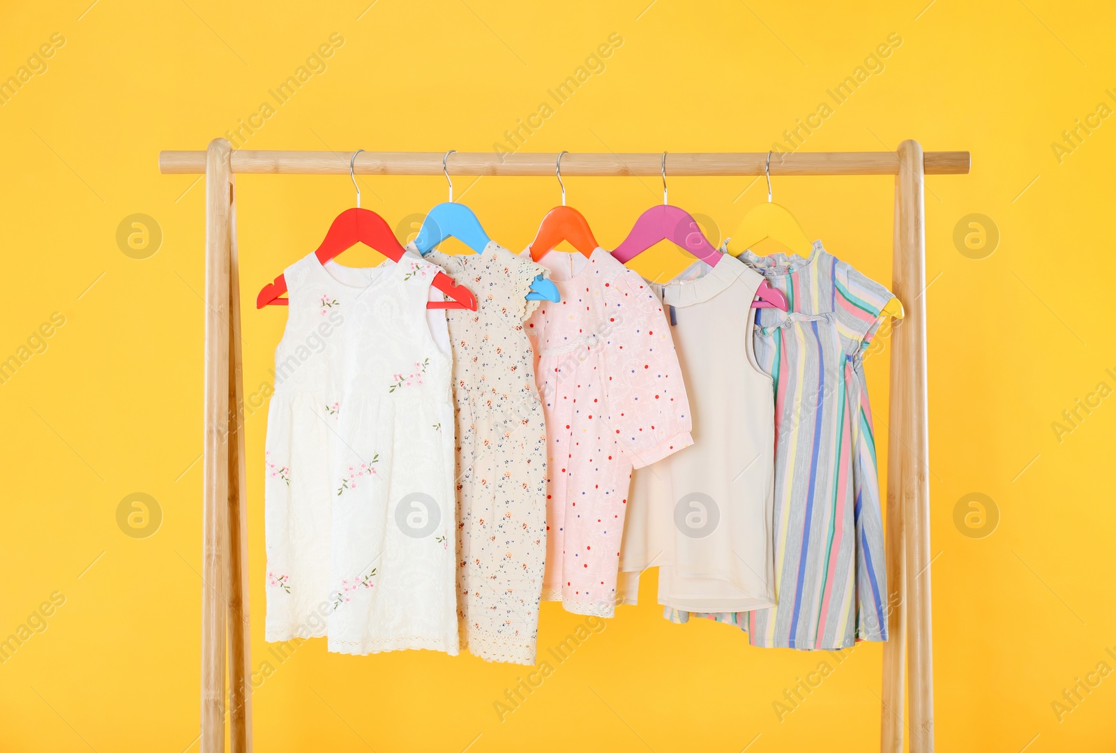 Photo of Rack with stylish children clothes on yellow background