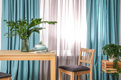 Photo of Stylish wooden table and chair near window with elegant curtains in room