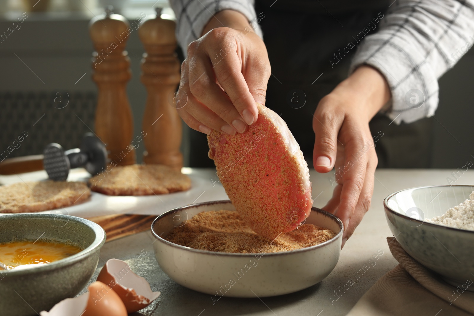 Photo of Woman cooking schnitzel at grey table indoors, closeup