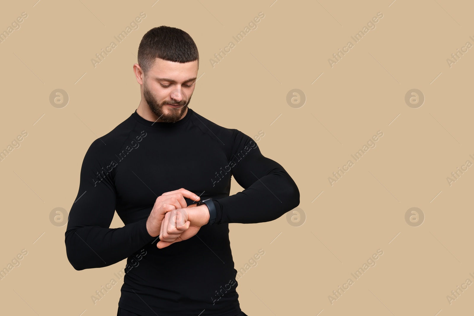 Photo of Handsome man checking fitness tracker on brown background, space for text