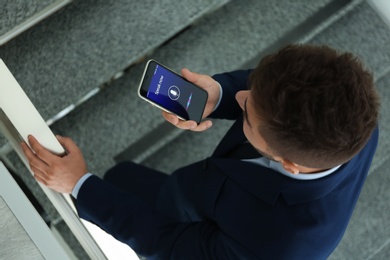 Photo of Young man using voice search on smartphone indoors, above view