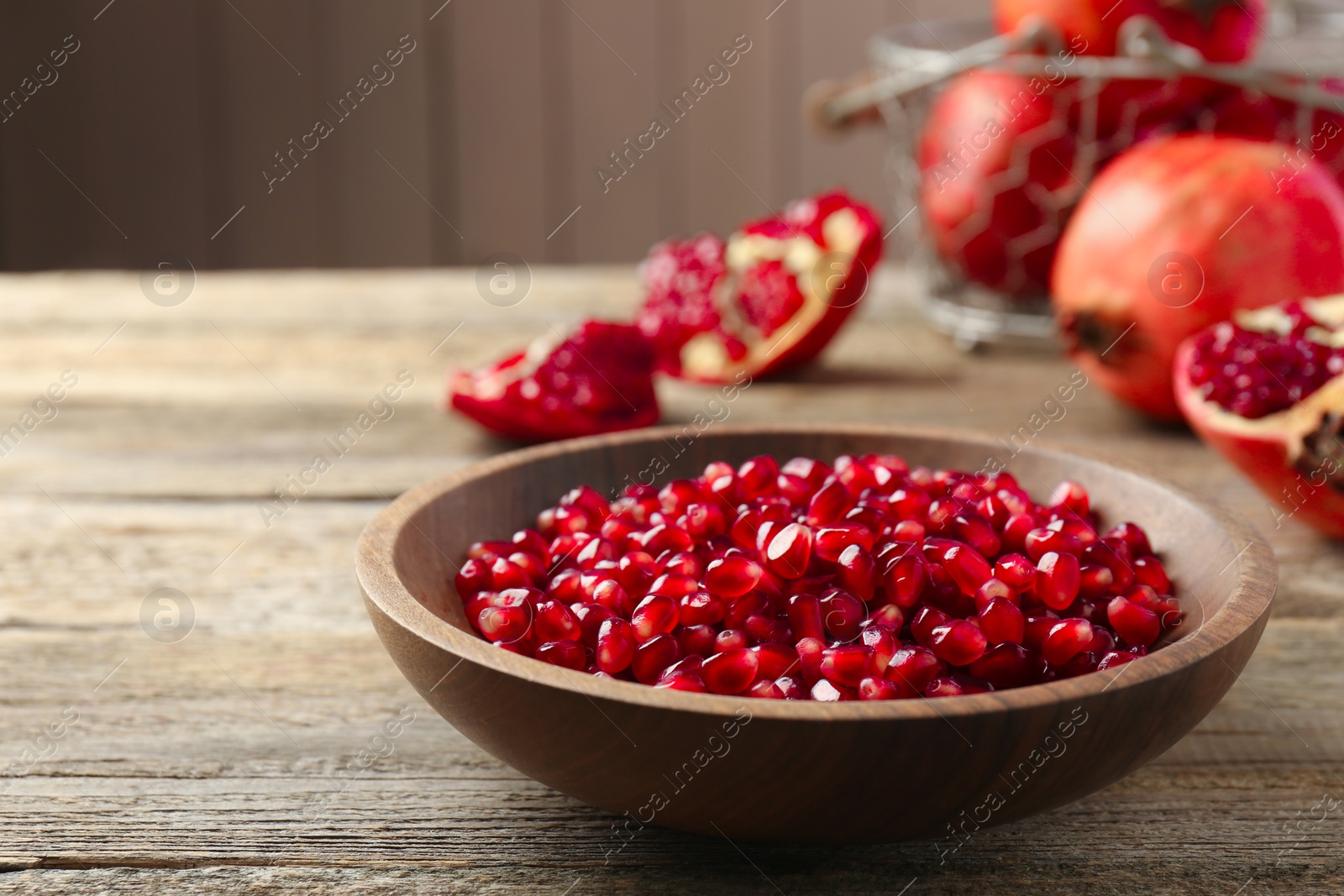 Photo of Ripe juicy pomegranate grains in bowl on wooden table. Space for text