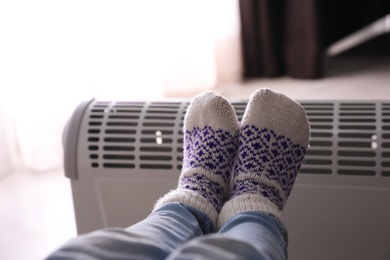 Photo of Child warming feet on electric heater at home, closeup