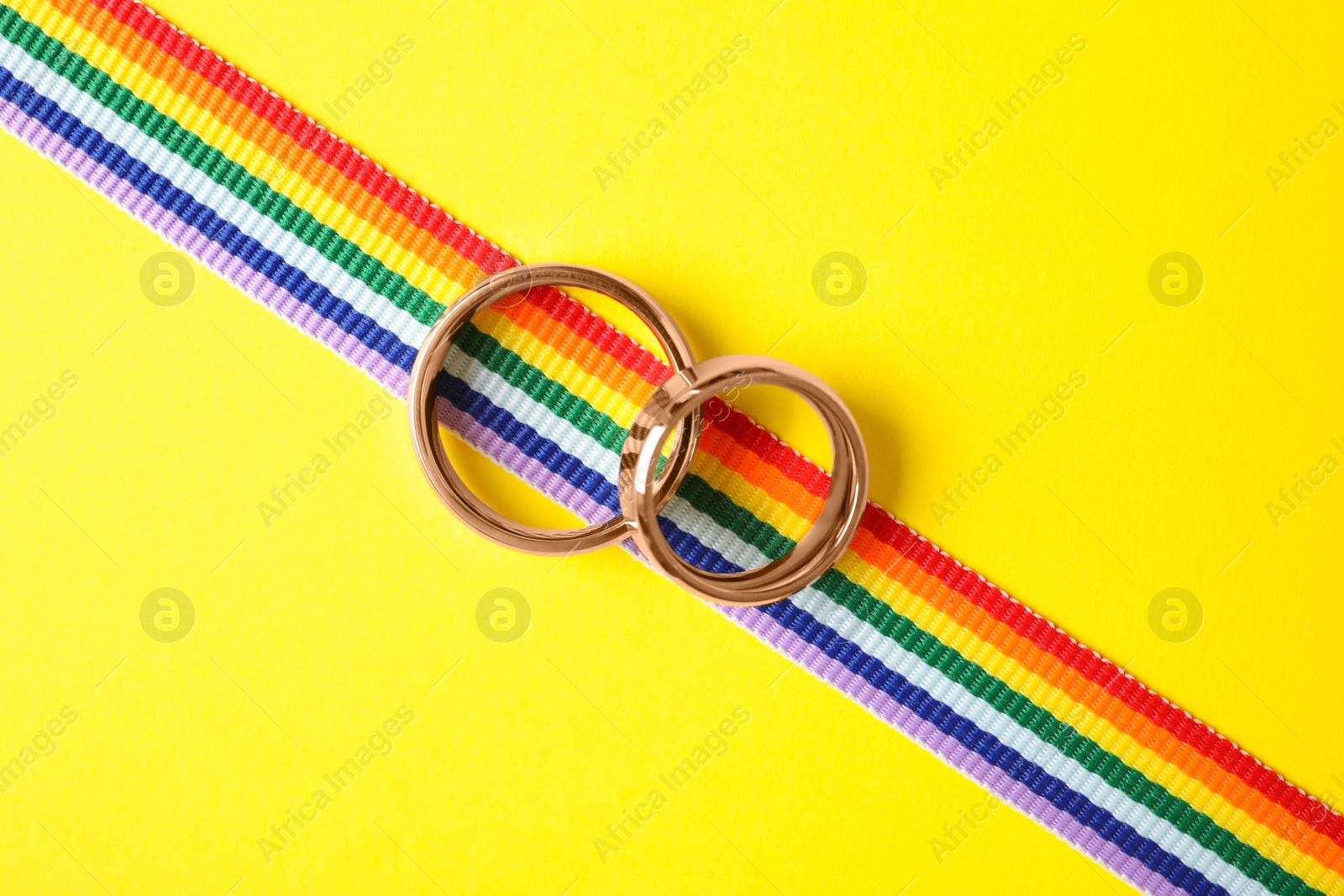 Photo of Wedding rings and rainbow ribbon on color background, top view. Gay symbol