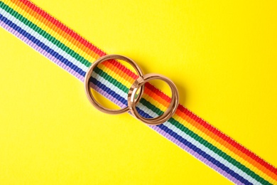 Wedding rings and rainbow ribbon on color background, top view. Gay symbol