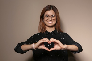 Photo of Woman showing HEART gesture in sign language on color background