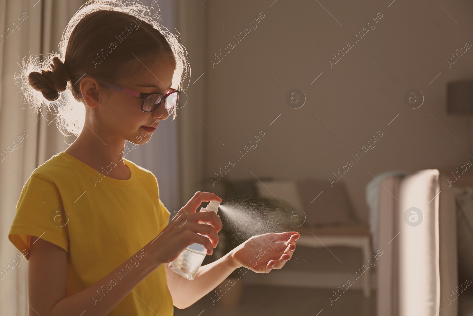 Photo of Little girl spraying antiseptic onto hand indoors. Space for text