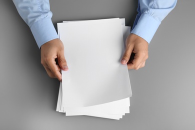 Photo of Man holding blank paper sheets for brochure at grey table, top view. Mock up