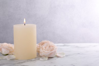 Spa composition with burning candle and flowers on white marble table, space for text