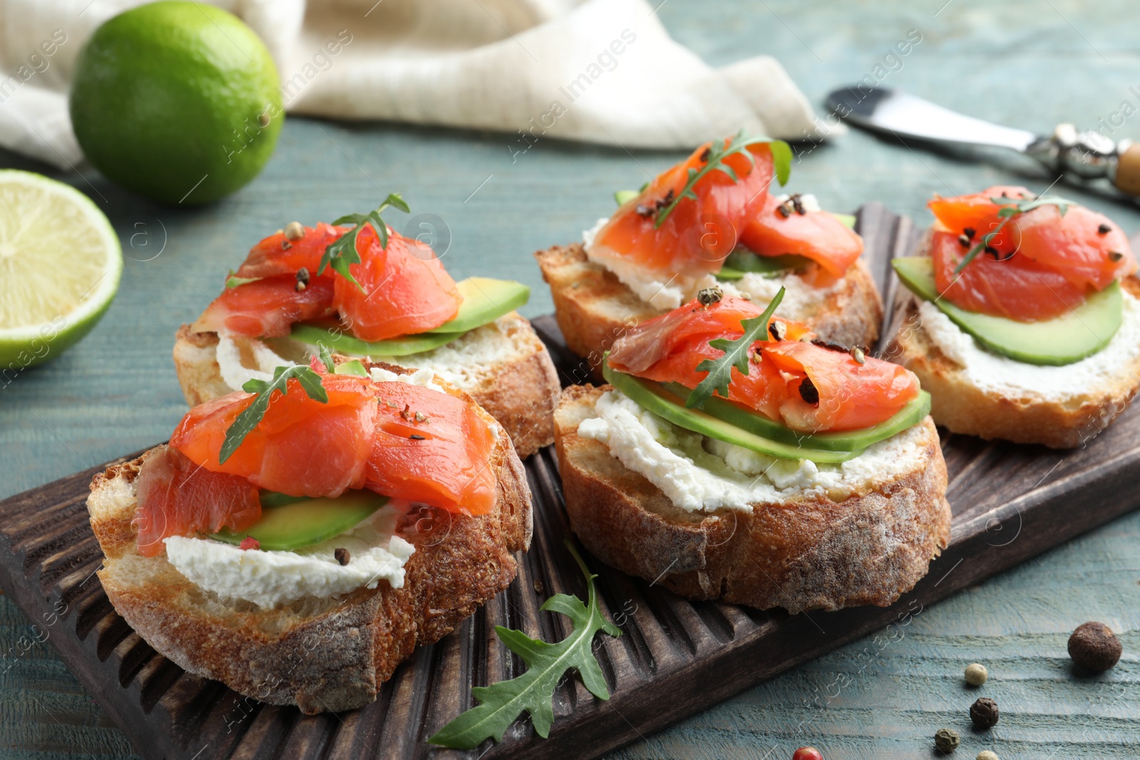 Photo of Delicious sandwiches with cream cheese, salmon, avocado and arugula on light blue wooden table, closeup