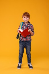 Photo of Smiling schoolboy with backpack and book on orange background