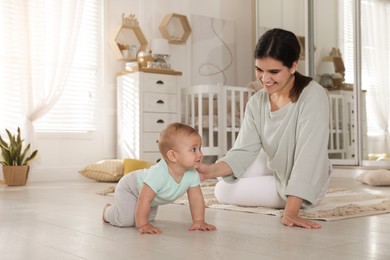 Photo of Happy young mother helping her cute baby to crawl on floor at home