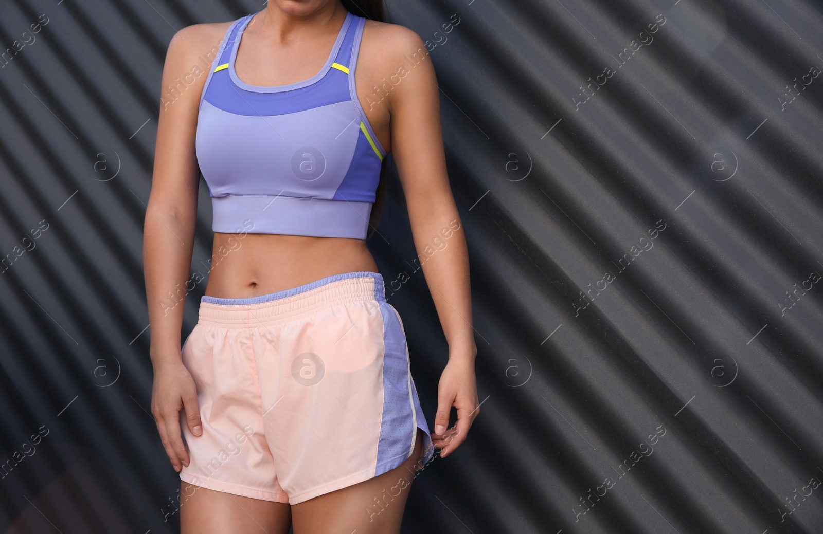 Photo of Young woman in sportswear near corrugated metal wall, closeup. Space for text