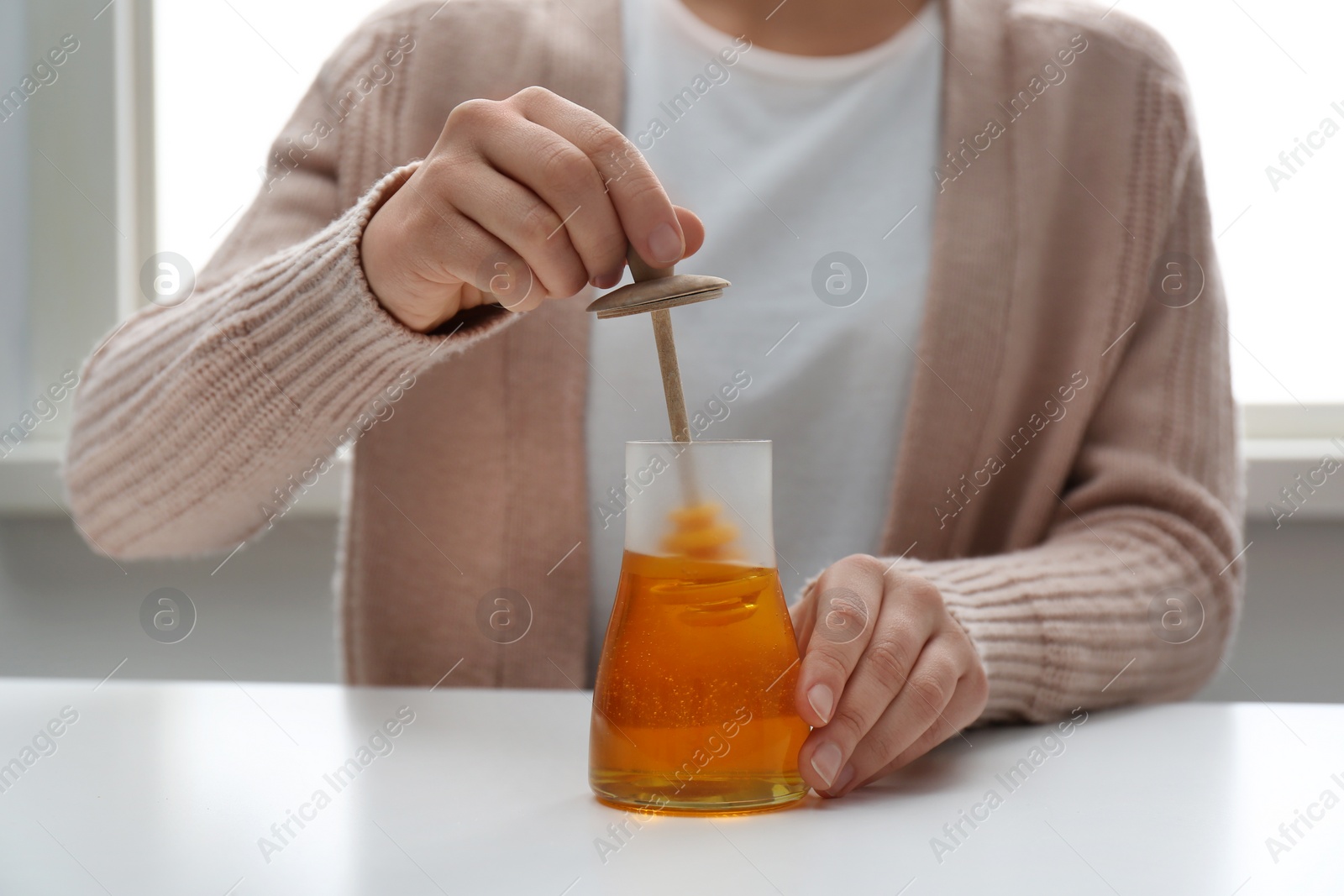 Photo of Woman with honey and dipper at white table, closeup