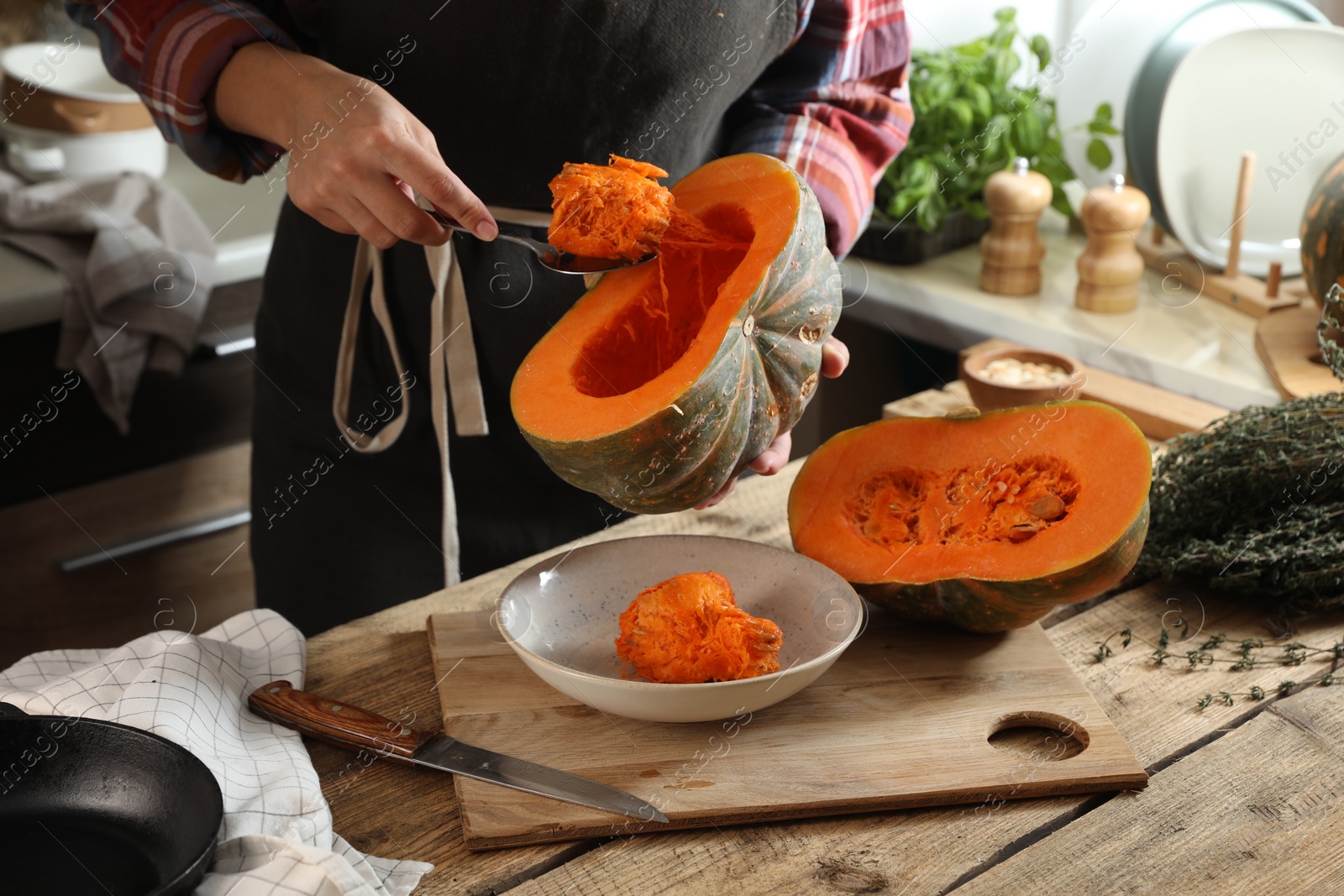 Photo of Woman removing seeds from raw pumpkin at wooden table in kitchen, closeup