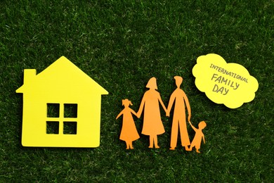 Photo of Card with text International Family Day, paper cutout and wooden house figure on green grass, flat lay