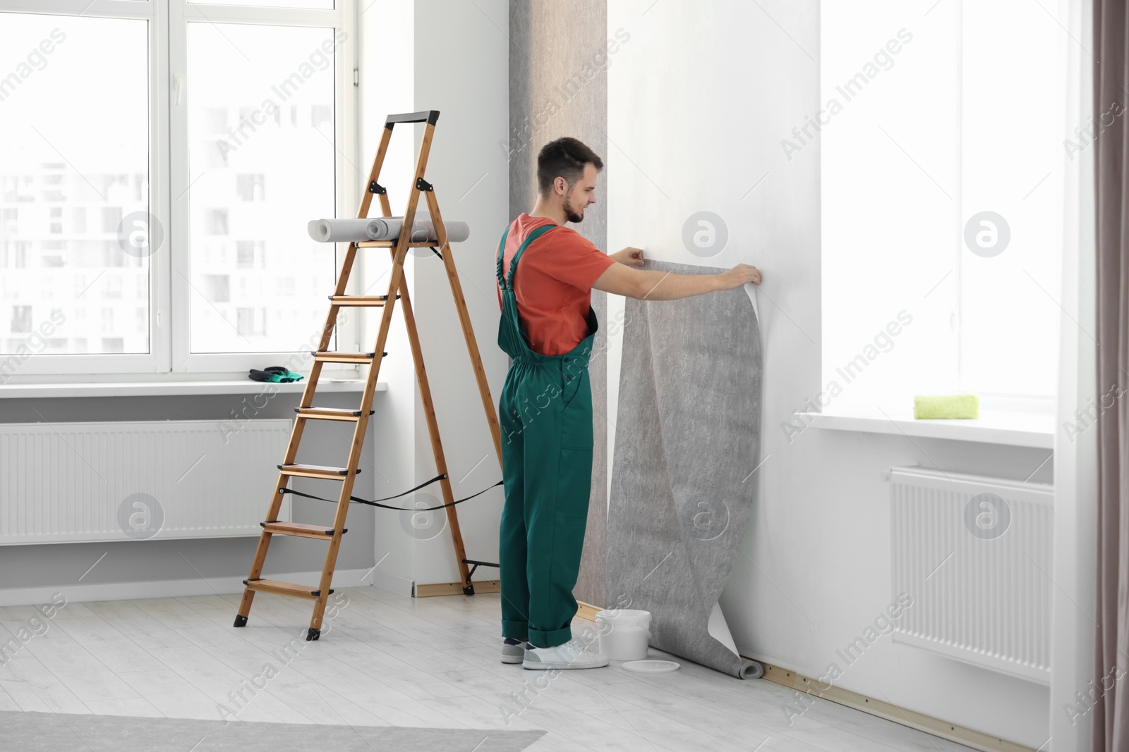 Photo of Man hanging stylish gray wallpaper in room