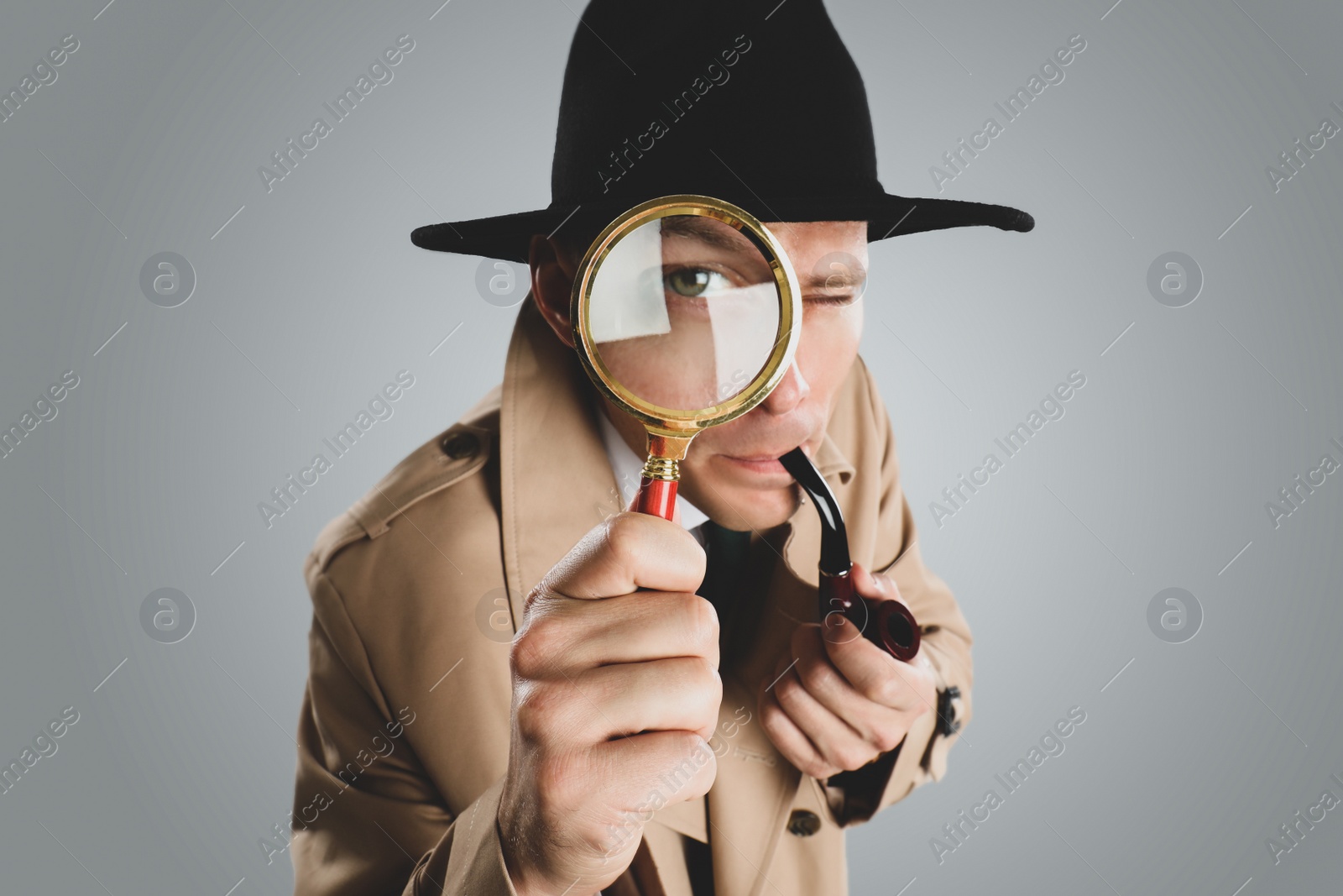 Photo of Male detective with smoking pipe looking through magnifying glass on grey background, closeup
