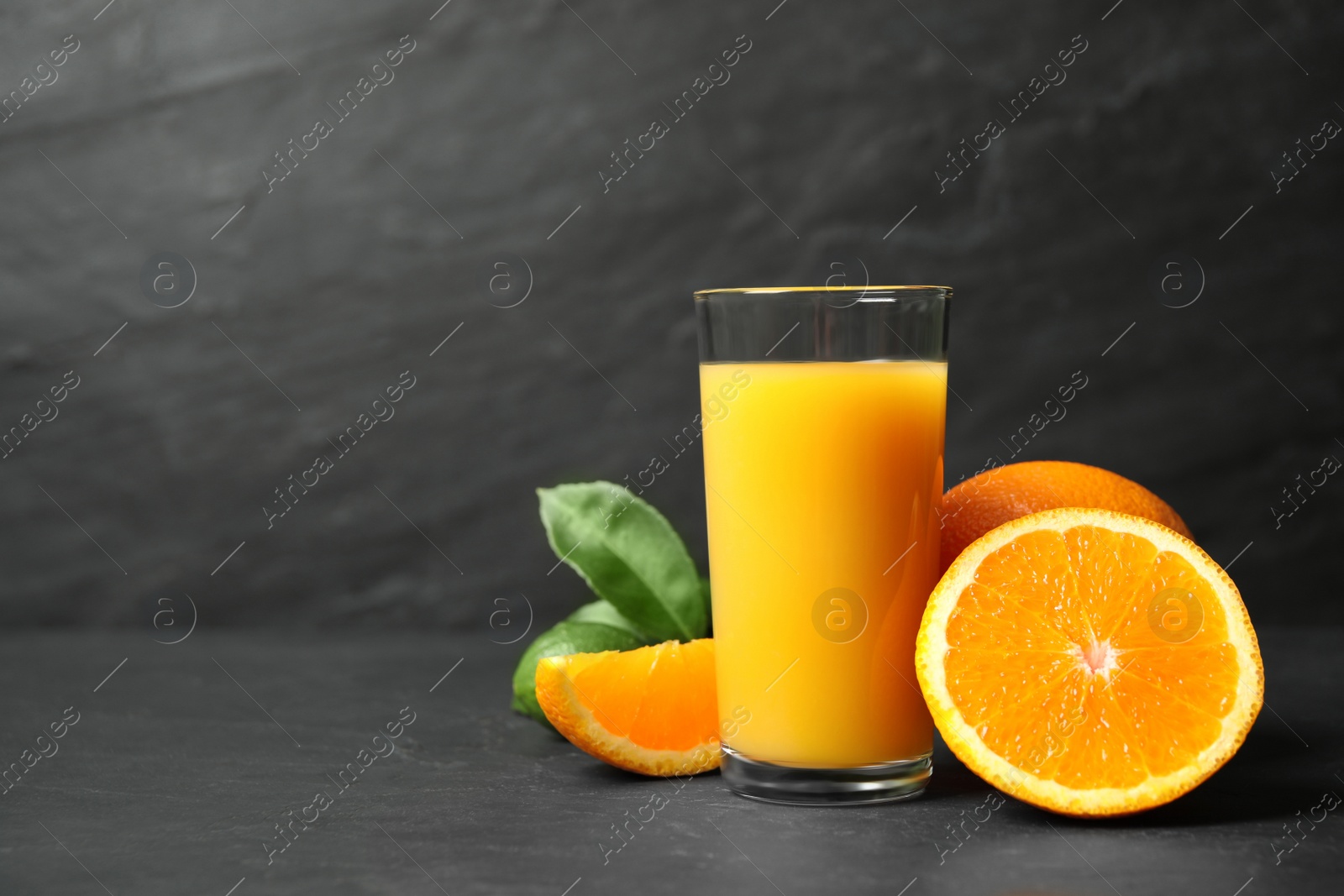 Photo of Glass of orange juice and fresh fruits on grey table. Space for text