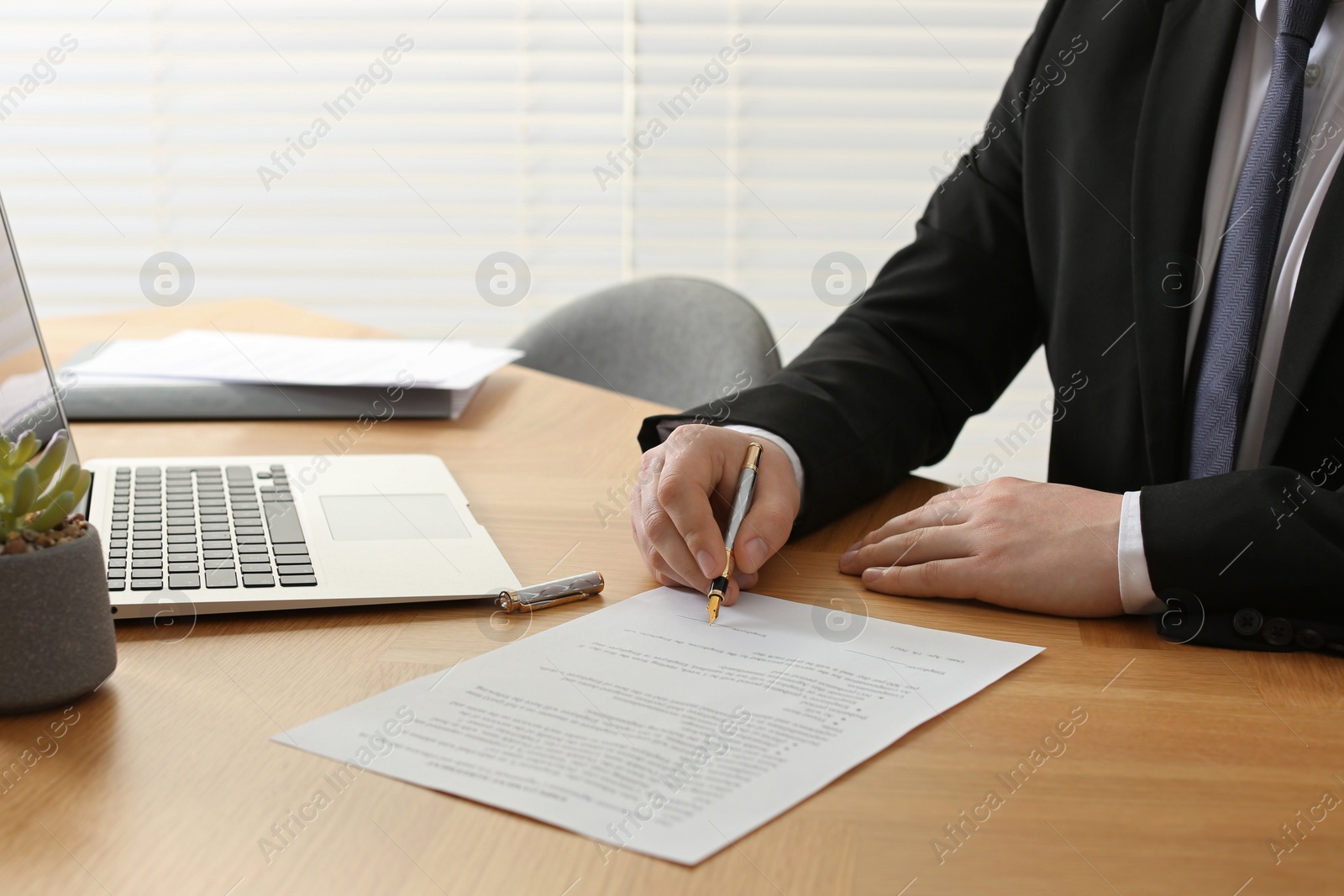 Photo of Notary signing document at wooden table indoors, closeup