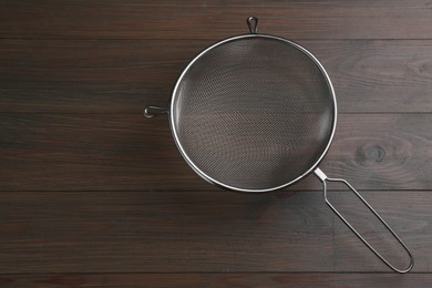 Photo of One metal sieve on wooden table, top view. Space for text