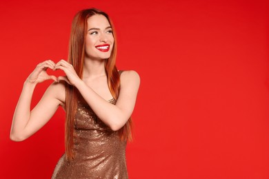 Photo of Young woman in dress making heart with hands on red background, space for text