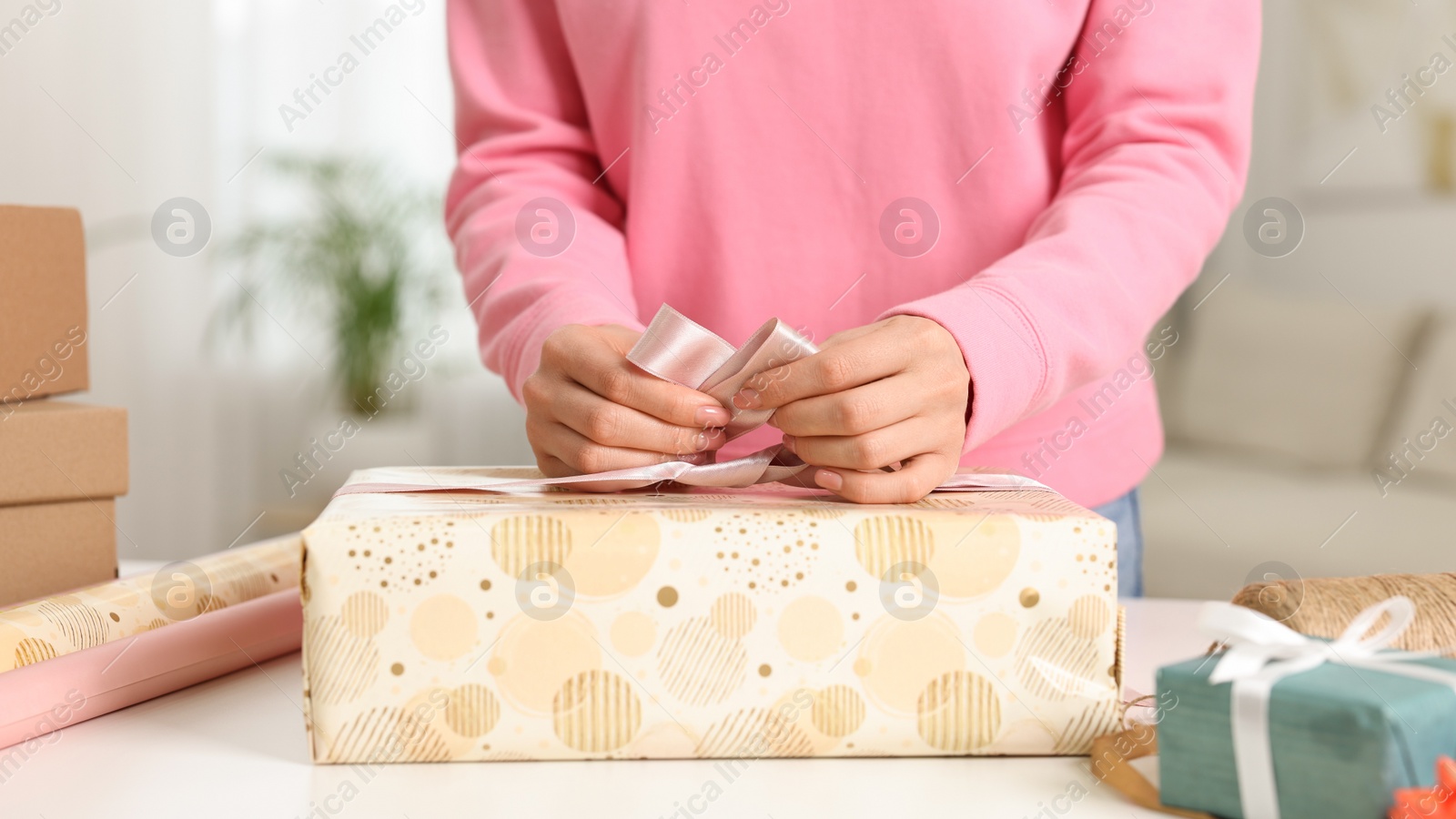 Photo of Woman wrapping gift at white table indoors, closeup