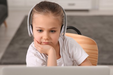 Little girl in headphones using laptop at home. Internet addiction